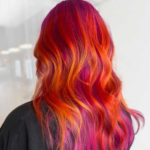 Vibrant hair with pink, orange, and red shades, styled in soft waves.