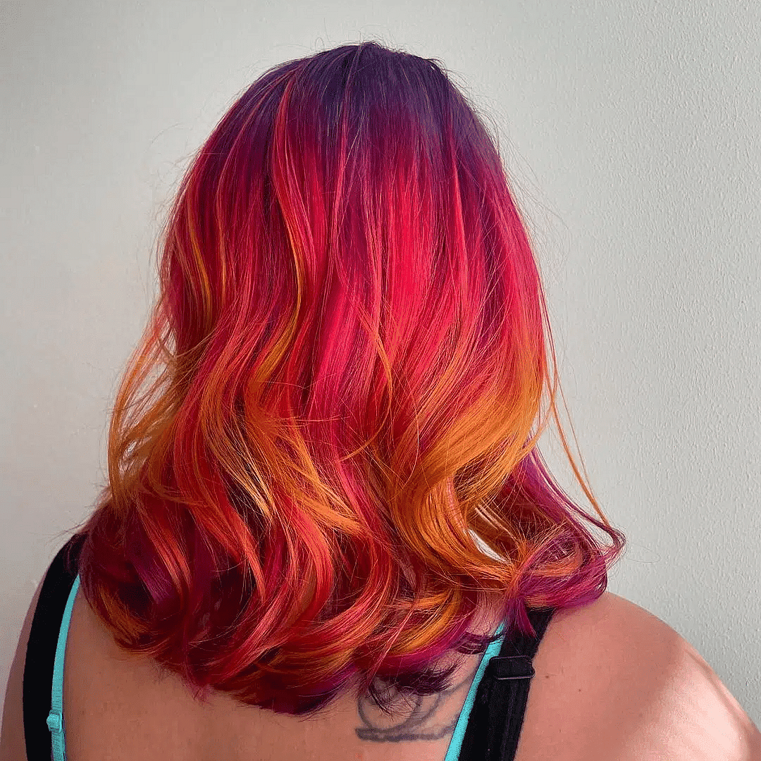 Person with vibrant, multi-colored hair in shades of purple, red, pink, and orange, seen from behind.