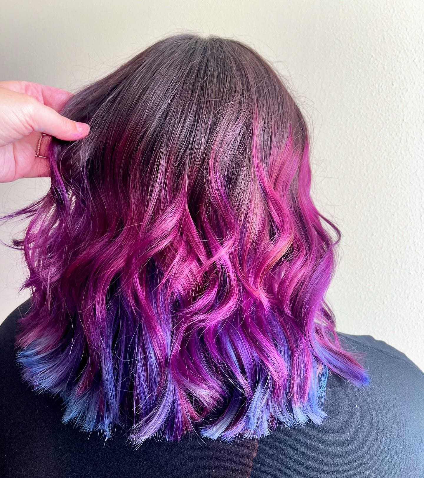 Woman with wavy hair dyed in shades of pink, purple, and blue, styled into loose curls.