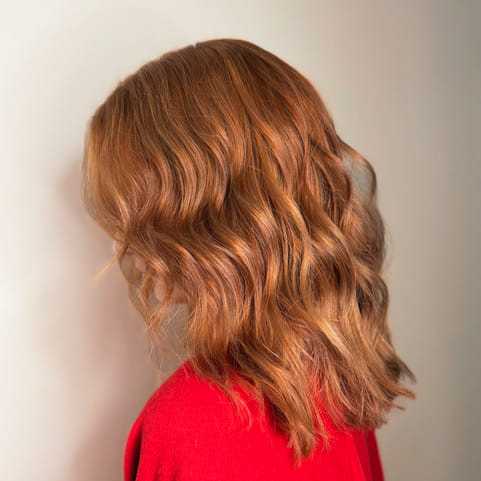 Wavy red hair cascading over shoulders, person in red sweater, facing away.