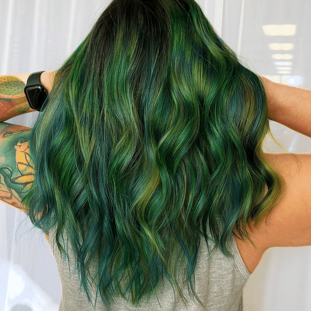 Person with long, wavy hair dyed in green and blue shades, holding it up to show underneath layers.