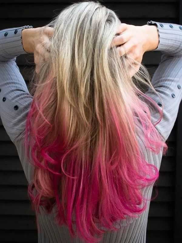 Woman with long blonde hair dyed pink at the ends, hands touching the back of her head.